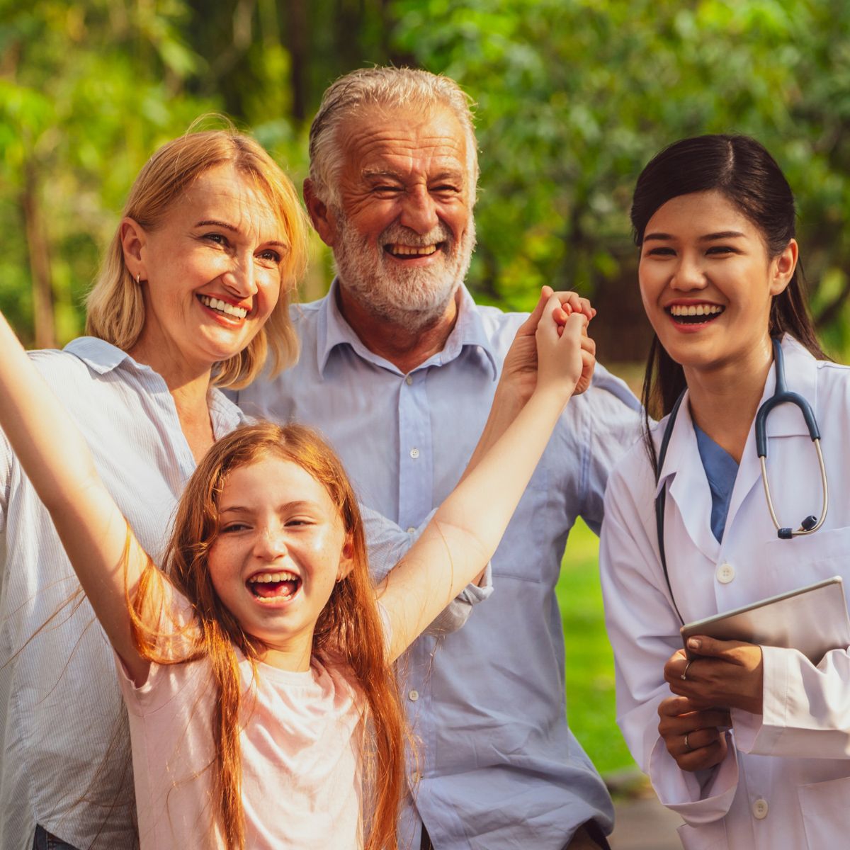 A happy family with a young girl, an older couple, and a doctor standing together outdoors, smiling and celebrating.
